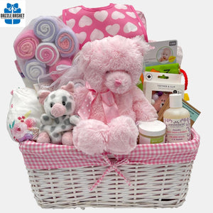 A baby girl gift basket that includes pink color themed baby products including blanket, onesie, baby care and a beautiful teddy bear packed in a lovely white basket.
