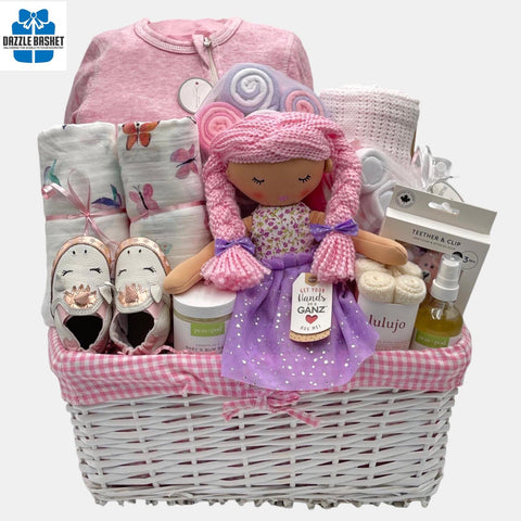A baby girl gift basket that includes pink colored baby products including blanket, onesie, shoes and a beautiful baby doll packed in a lovely white basket.