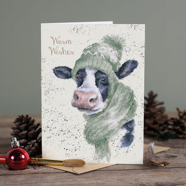 A Christmas greeting card that features a cow wearing winter clothes