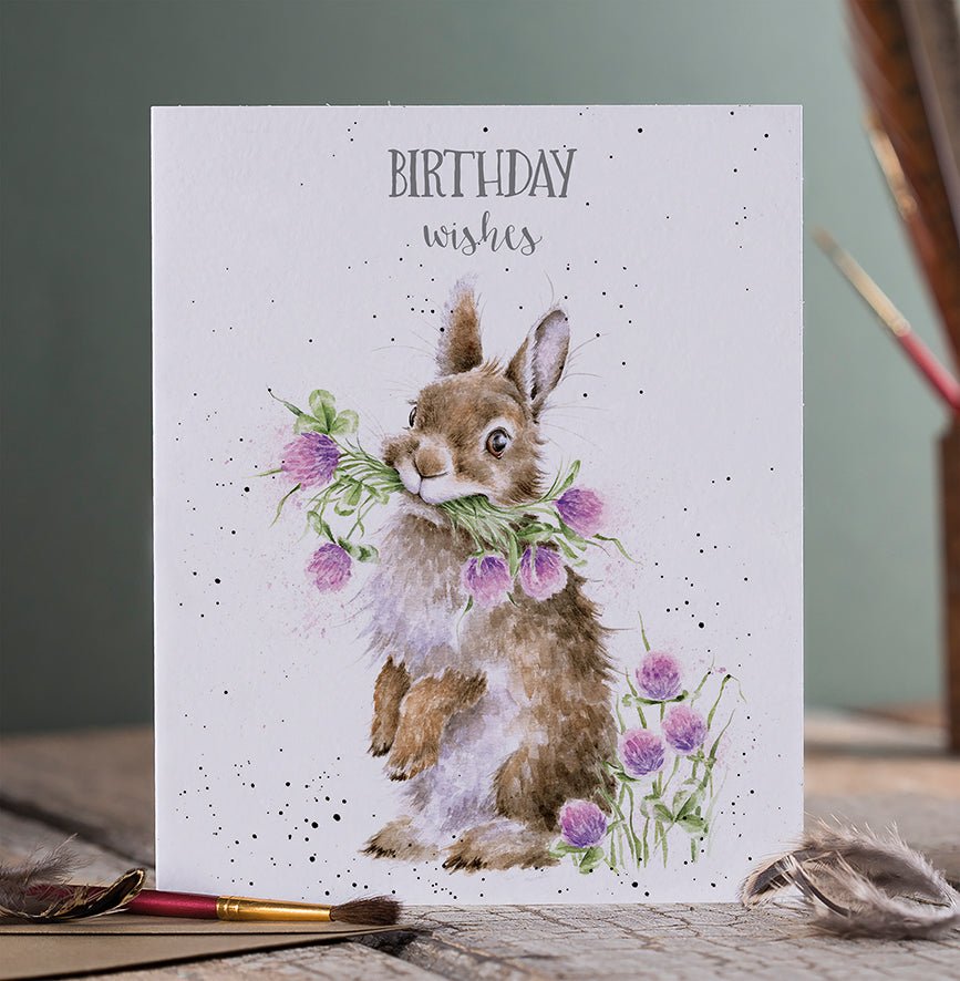 A birthday greeting card with picture of a bunny holding bunch of purple wildflowers.