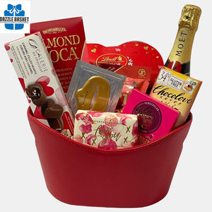 Love Gift baskets Calgary from Dazzle Basket- A red color themed valentine gift basket that includes a bottle of champagne and delicious gourmet snacks including a love soap and chocolates made in a red faux leather oval container
