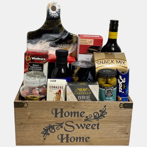 A made in Calgary Housewarming gift basket filled with tasty gourmet treats and useful products such as cheeseboard, travel tumbler, fancy wine corker etc. packed in a wooden basket titled "Home Sweet Home".
