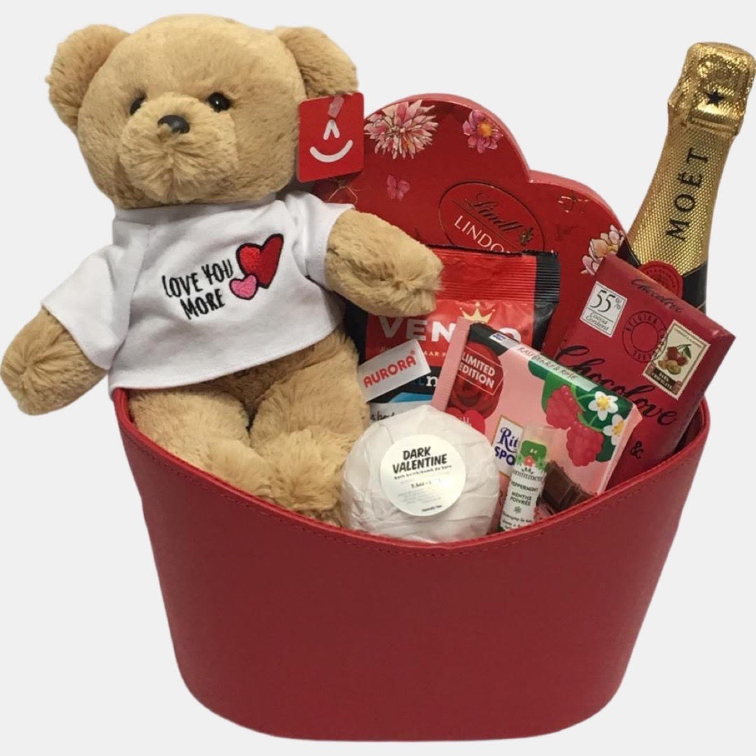 A red color themed valentine gift basket that includes a bottle of champagne, "Love you More"  teddy bear and delicious gourmet snacks including cheese and chocolates made in a red faux leather oval container